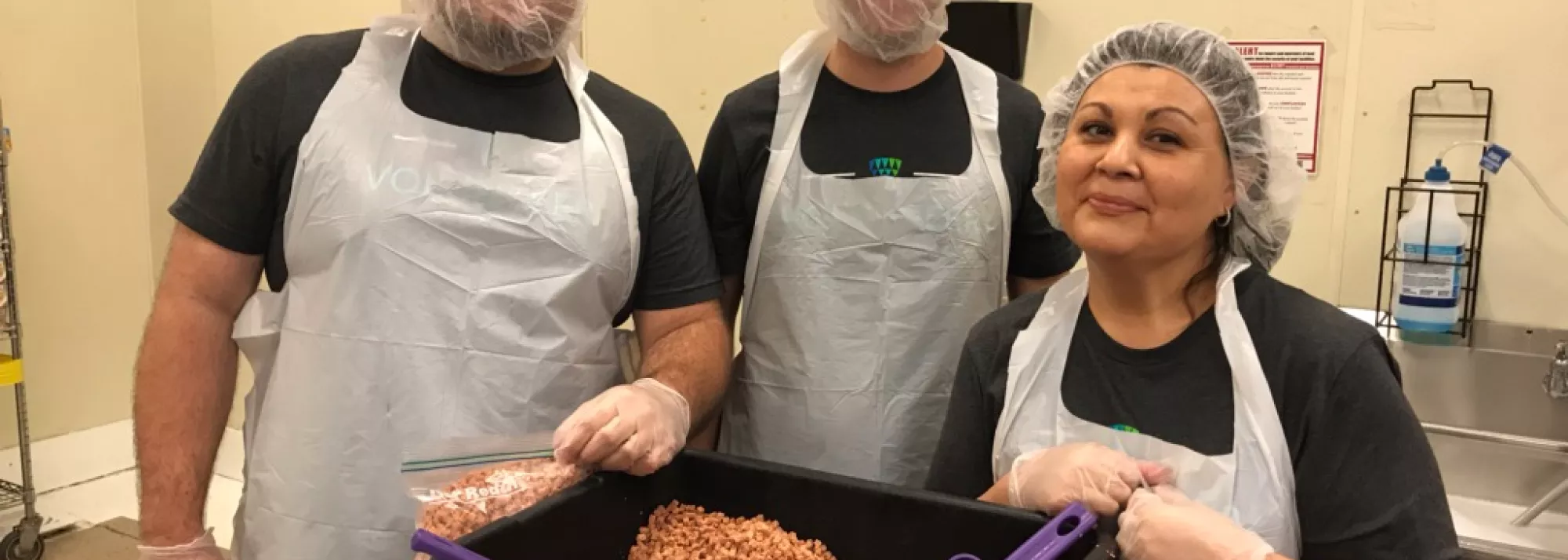 Three Lineage volunteers pose for a photo while scooping pepperoni at a food bank